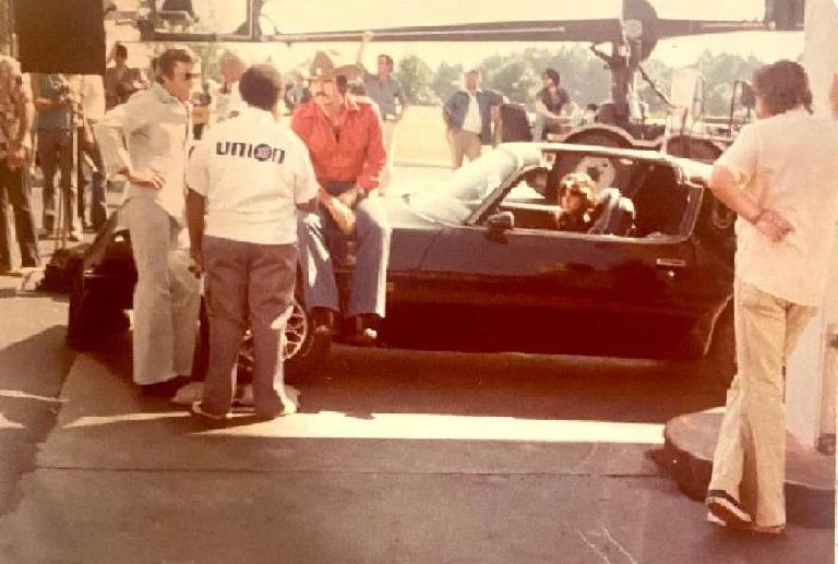 Smokey and the Bandit movie behind the scenes pic with Burt Reynolds at the gas station. Burt sits on the hood and the attendant says, 'Trans Am !! What's your pleasure ?':
